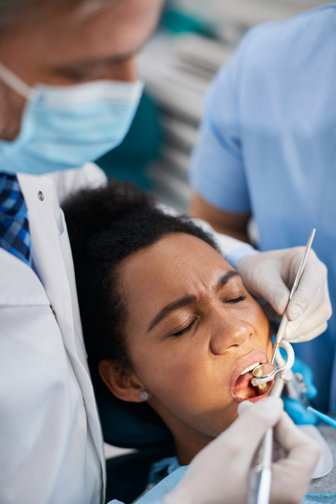 Black woman holding her eyes closed during dental procedure at dentist's office.