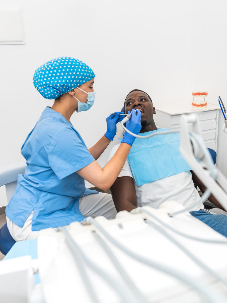 Dental hygienist performing a dental checkup using modern tools on an African male patient.